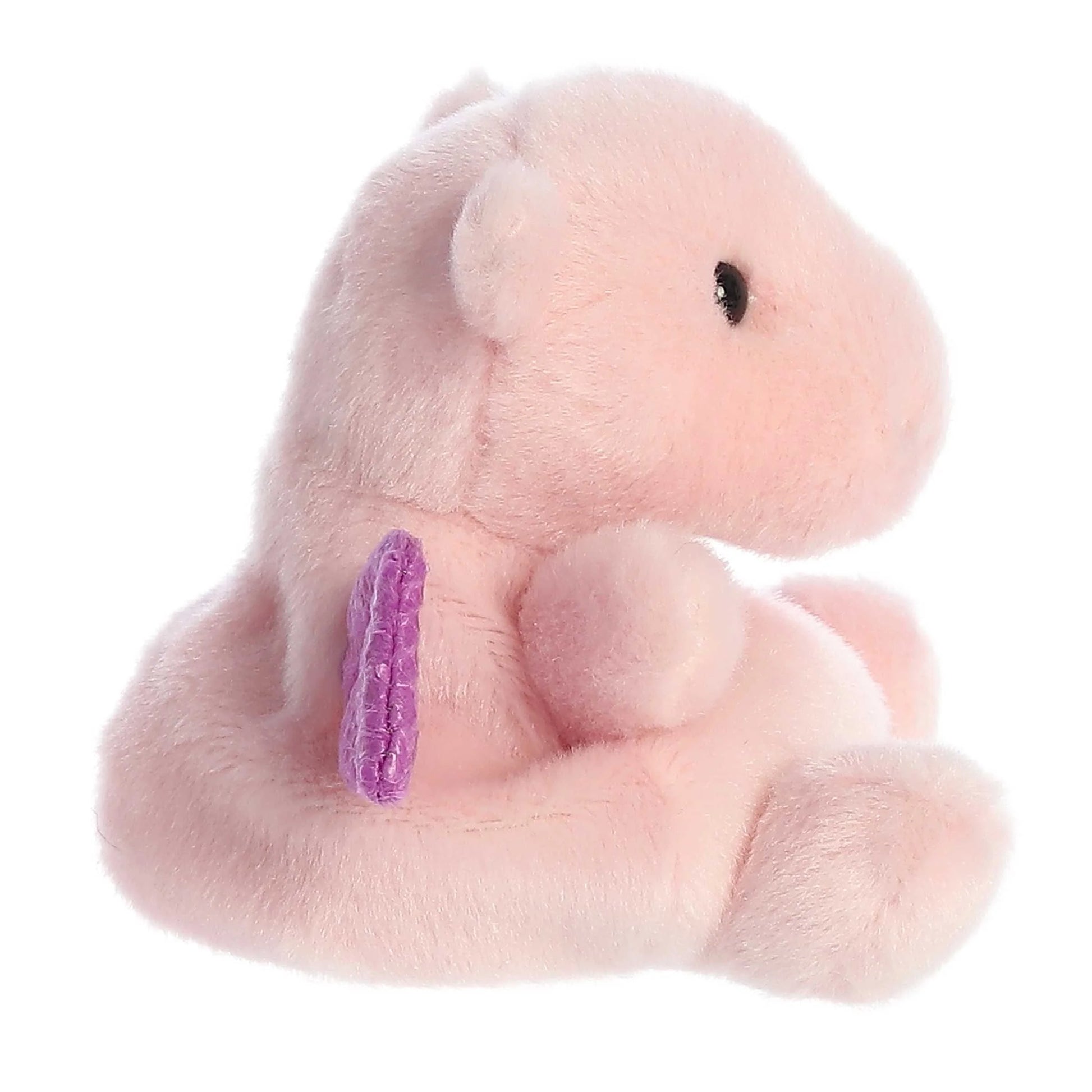 Side View of A small, soft pink plush dragon (Palm Pals Aria) sitting down, with shiny, textured purple wings and small black eyes.