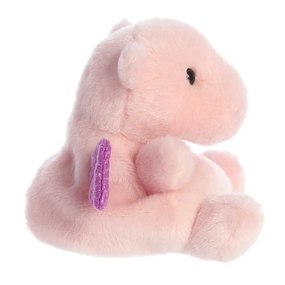 Side View of A small, soft pink plush dragon (Palm Pals Aria) sitting down, with shiny, textured purple wings and small black eyes.