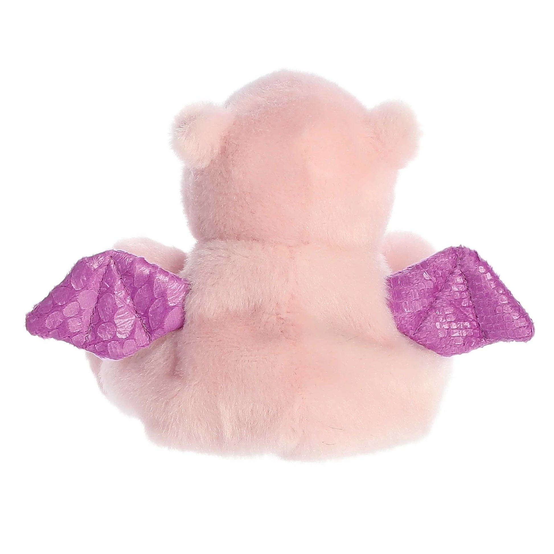 Back of A small, soft pink plush dragon (Palm Pals Aria) sitting down, with shiny, textured purple wings and small black eyes.