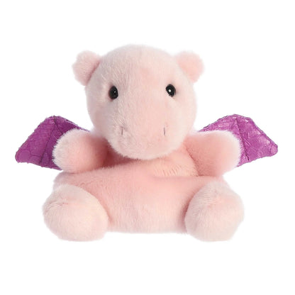 A small, soft pink plush dragon (Palm Pals Aria) sitting down, with shiny, textured purple wings and small black eyes.