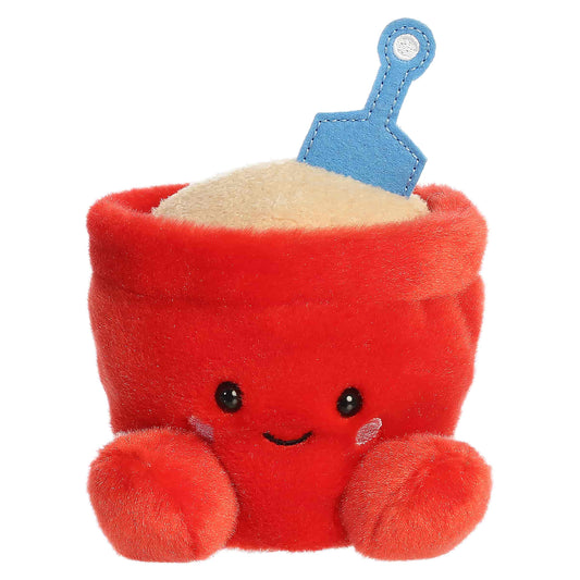 Palm Pals June Sand Bucket, a small red plush shaped like a beach bucket filled with sand and a blue shovel, featuring a sweet smiling face.