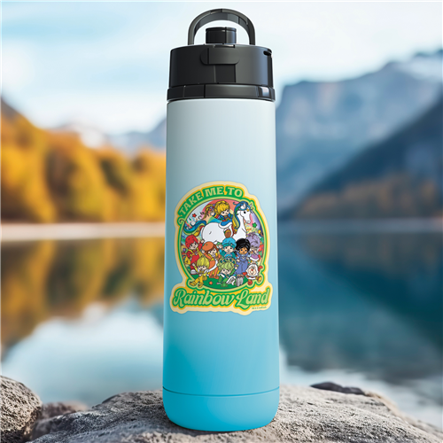 Blue water bottle with a colorful character design on a rock by a lake with mountains in the background
