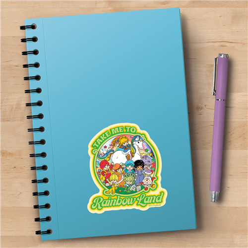 Notebook with 'Take Me to Rainbow Land' design on a wooden surface with a purple pen.
