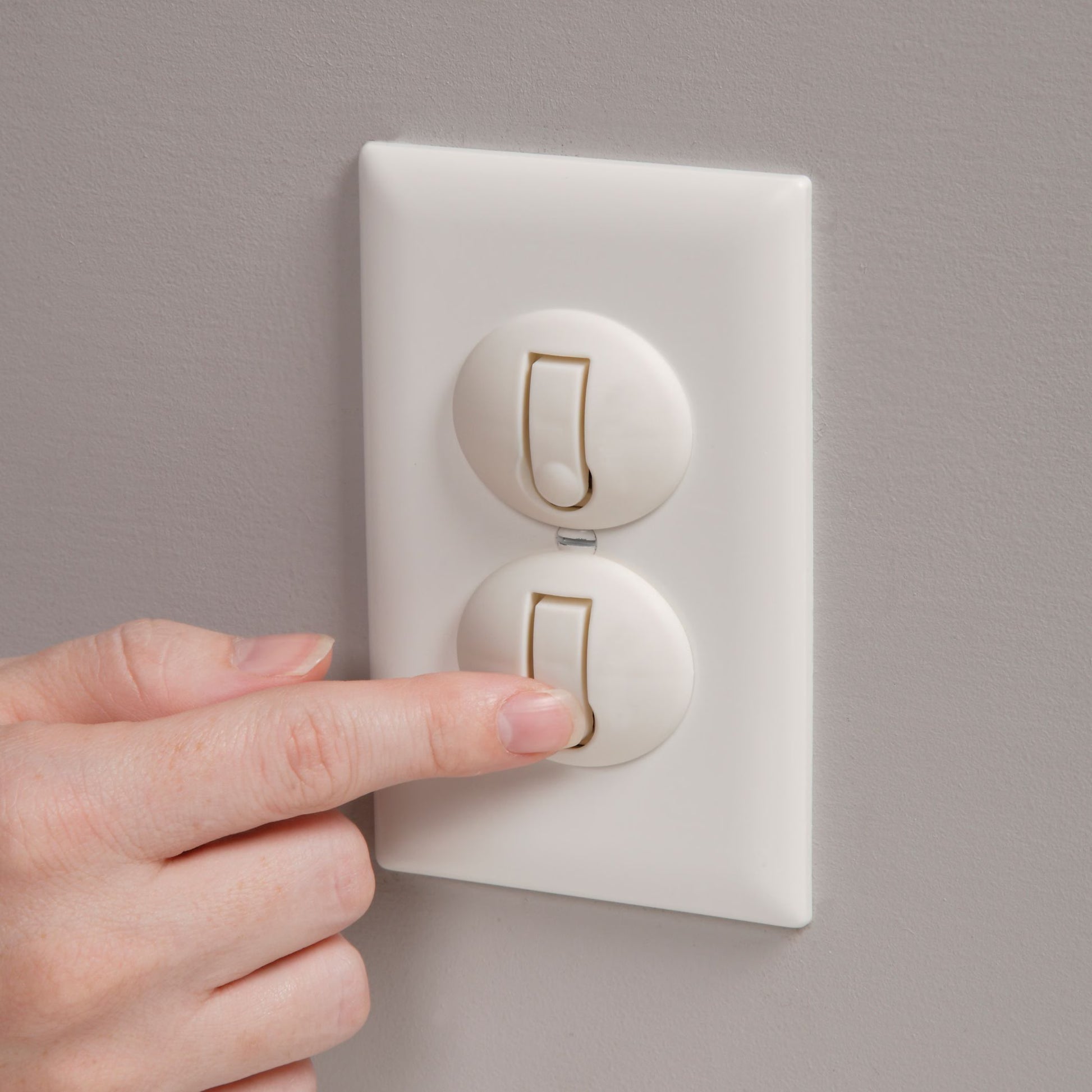 Hand pressing a light switch on a gray wall