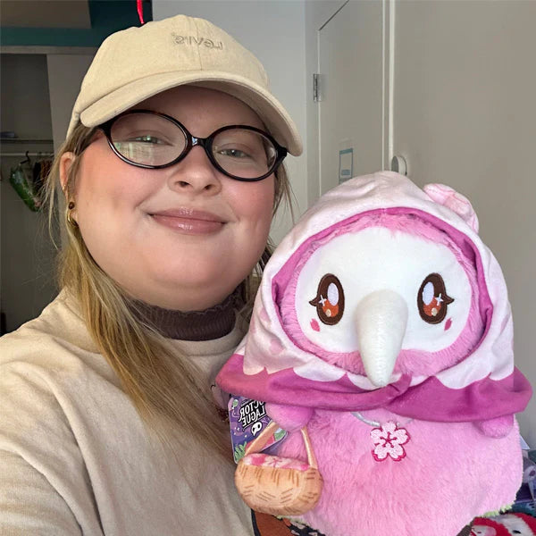 Person wearing a beige cap and glasses holding a pink plush toy.