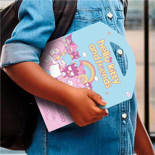 Person holding a colorful 'hello kitty and friends' book with a denim jacket and backpack.