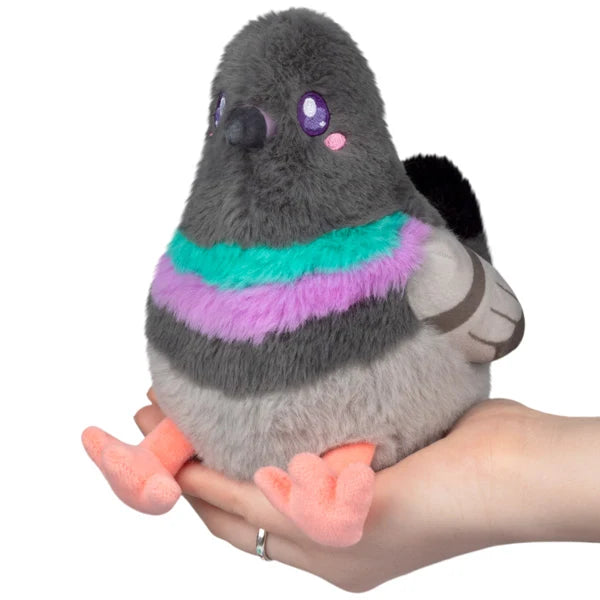 Squishable Snacker Pigeon S1E4 plush resting in hands, featuring soft grey fur, a bright purple and teal neck band, and little orange feet.