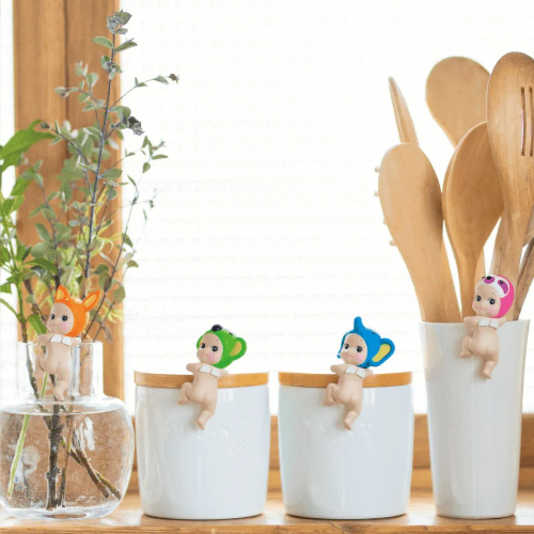 Four small white cups with decorative figures on a wooden surface, next to a vase with greenery.