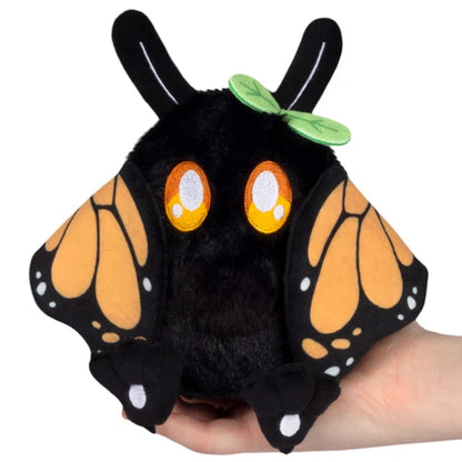 Squishable Alter Egos Series 21 Monarch Mothman plush with black fur, orange glowing eyes, a leaf accent, and monarch butterfly wings.