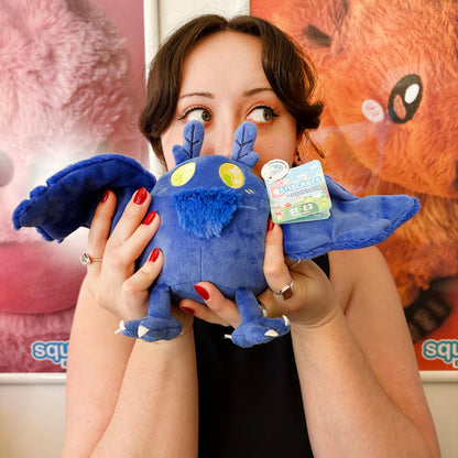 Person holding a blue plush toy with a visible brand label against a colorful background
