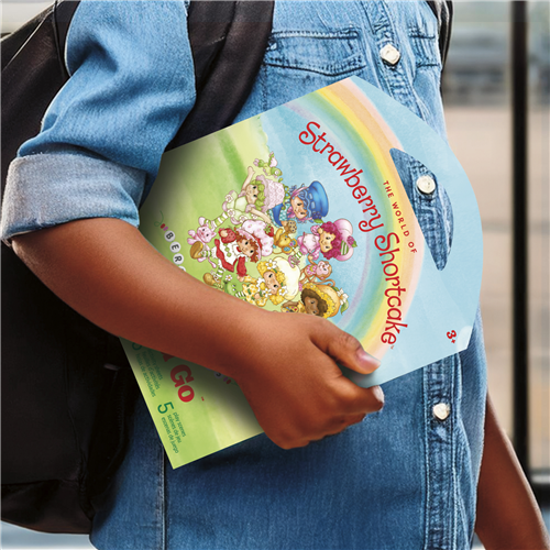 Child holding a colorful book titled 'Strawberry Shortcake' against a blurred background