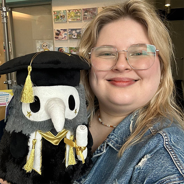 Squishable Mini Graduation Plague Doctor 10-Inch Plush, a black and dark grey soft toy with a white mask, gold accents, a graduation cap, and a diploma