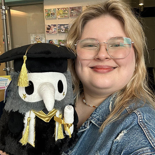 Squishable Mini Graduation Plague Doctor 10-Inch Plush, a black and dark grey soft toy with a white mask, gold accents, a graduation cap, and a diploma