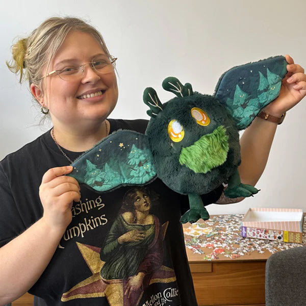 Person holding a plush toy with a forest design, wearing a black t-shirt with a graphic design.