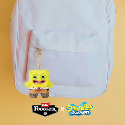 Yellow plush keychain with a red tie attached to a white backpack on a yellow background, featuring Fuggler and SpongeBob SquarePants logos.